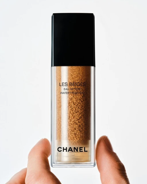 Tan tinted makeup in a clear bottle with a black lid held by a hand, against a white background, product shot for the beauty industry.