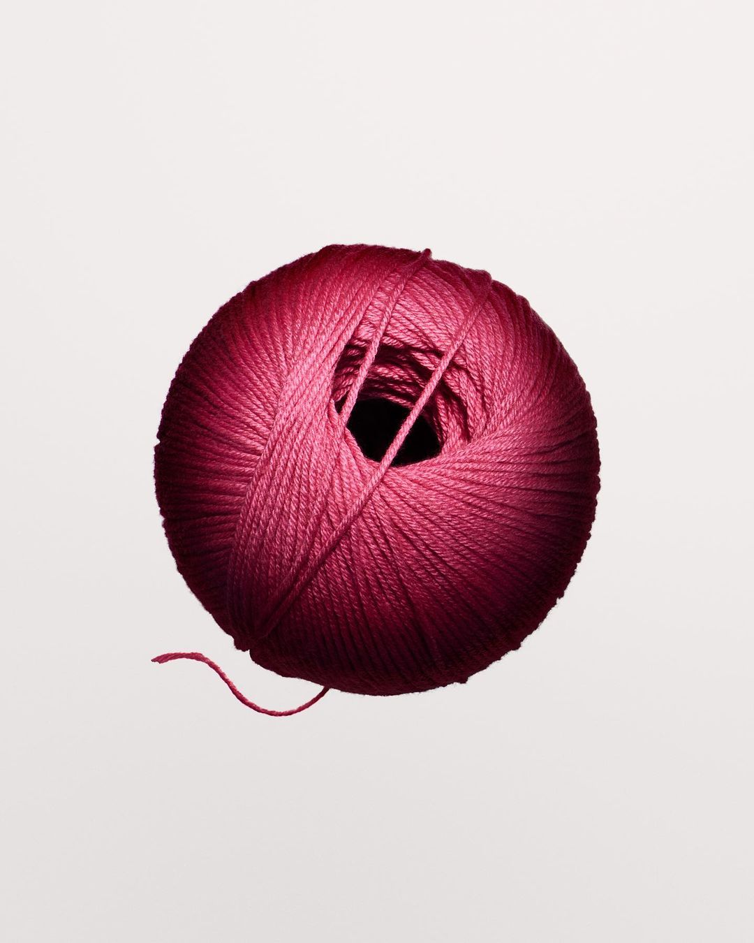 Close-up shot of a round ball of pink yarn against a white background, with the texture of the yarn clearly visible.