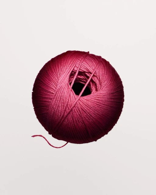 Close-up shot of a round ball of pink yarn against a white background, with the texture of the yarn clearly visible.