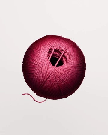 Close-up shot of a round ball of pink yarn against a white background, with the texture of the yarn clearly visible.