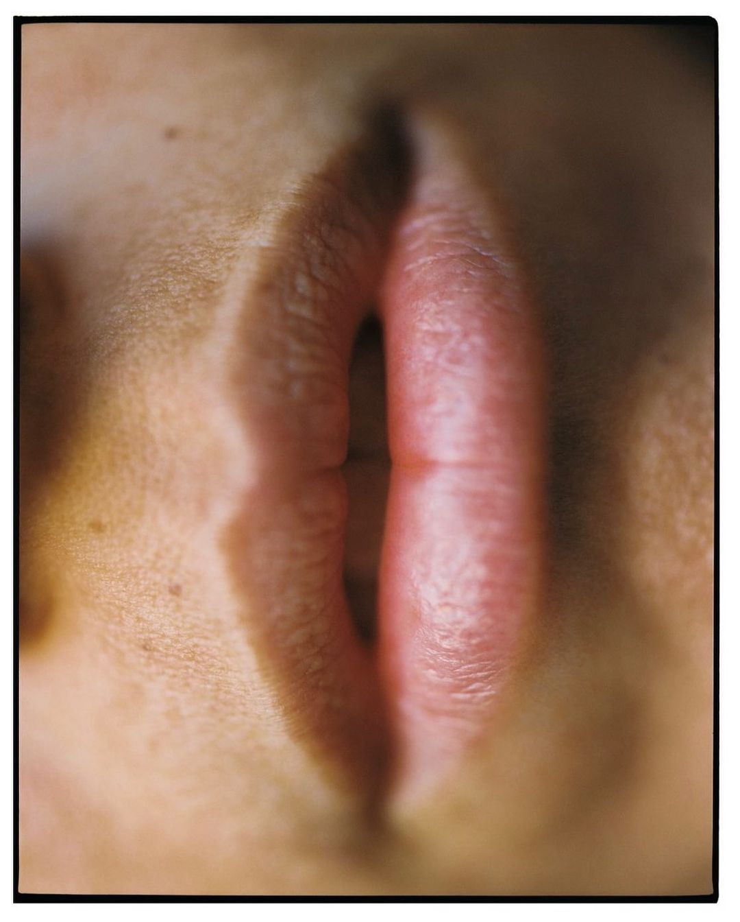 Close-up studio shot of a person's closed lips, focusing on their texture and form. The light source creates soft shadows.