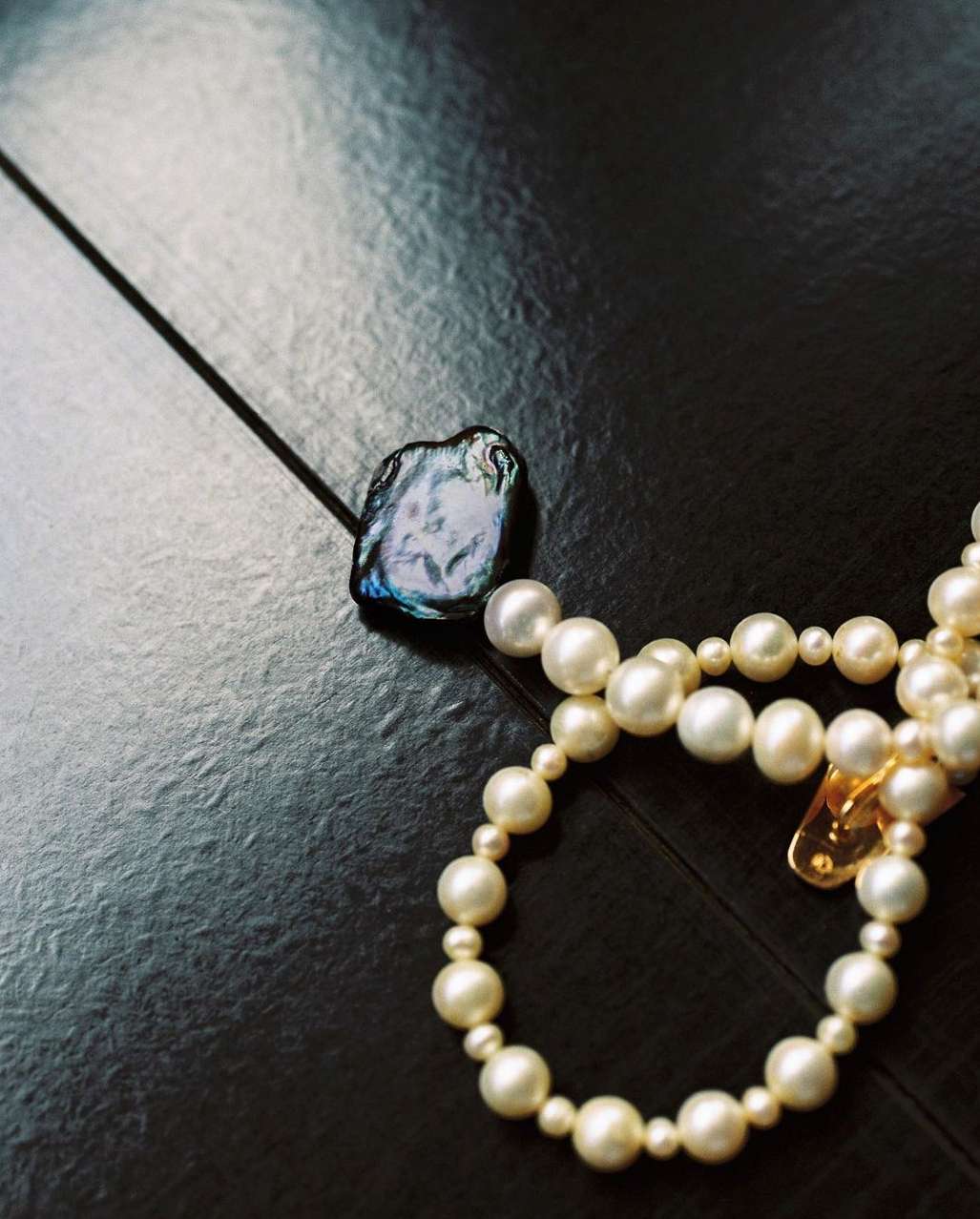 Close-up of a baroque pearl necklace on a dark surface, featuring white pearls and an irregular pearl pendant with iridescent reflections.