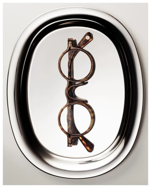 Optical eyeglasses with tortoise shell frames are displayed on an oval silver tray against a light backdrop in a studio shot.