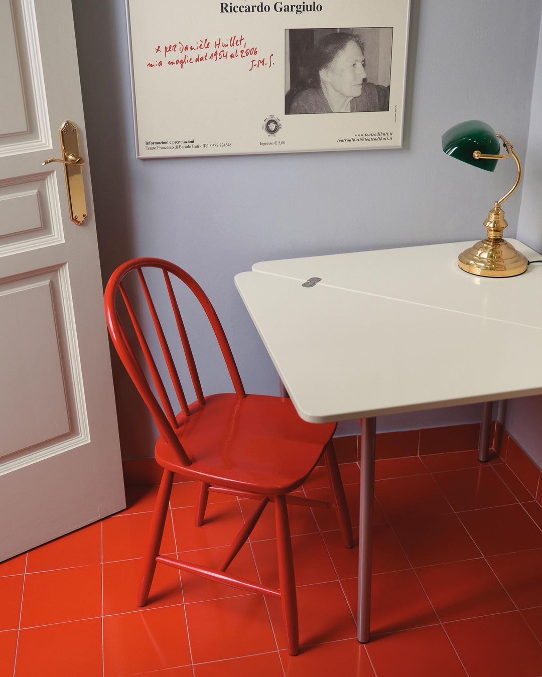 Interior view of a room with a red chair, white table, and a poster on the wall, captured in a brightly lit, cozy, and functional setting.