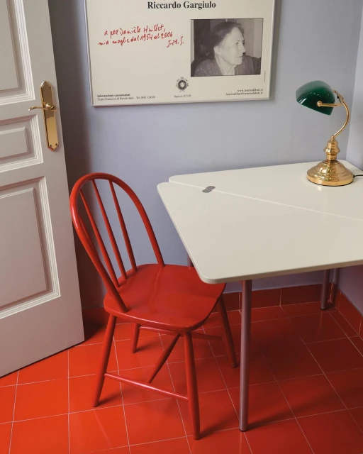 Interior view of a room with a red chair, white table, and a poster on the wall, captured in a brightly lit, cozy, and functional setting.