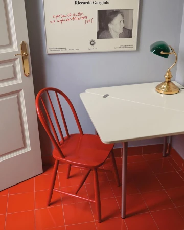 Interior view of a room with a red chair, white table, and a poster on the wall, captured in a brightly lit, cozy, and functional setting.