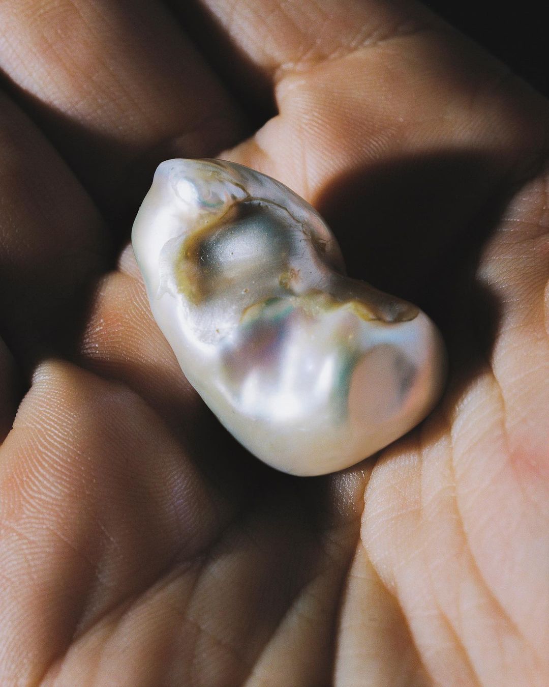 Close-up of a large, baroque pearl with an irregular shape, held in the palm of a person's hand, showcasing its unique luster and texture.