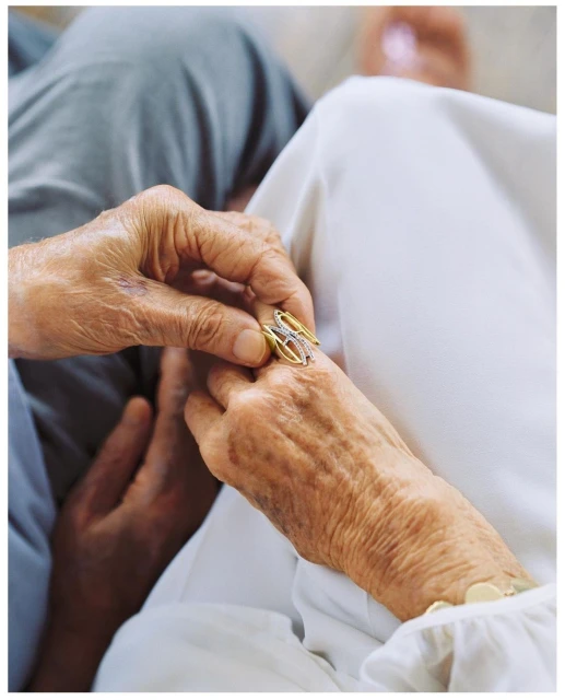 Close-up captures an elderly couple's hands, one gently placing a gold ring on the other's finger, symbolizing love and commitment in soft lighting.