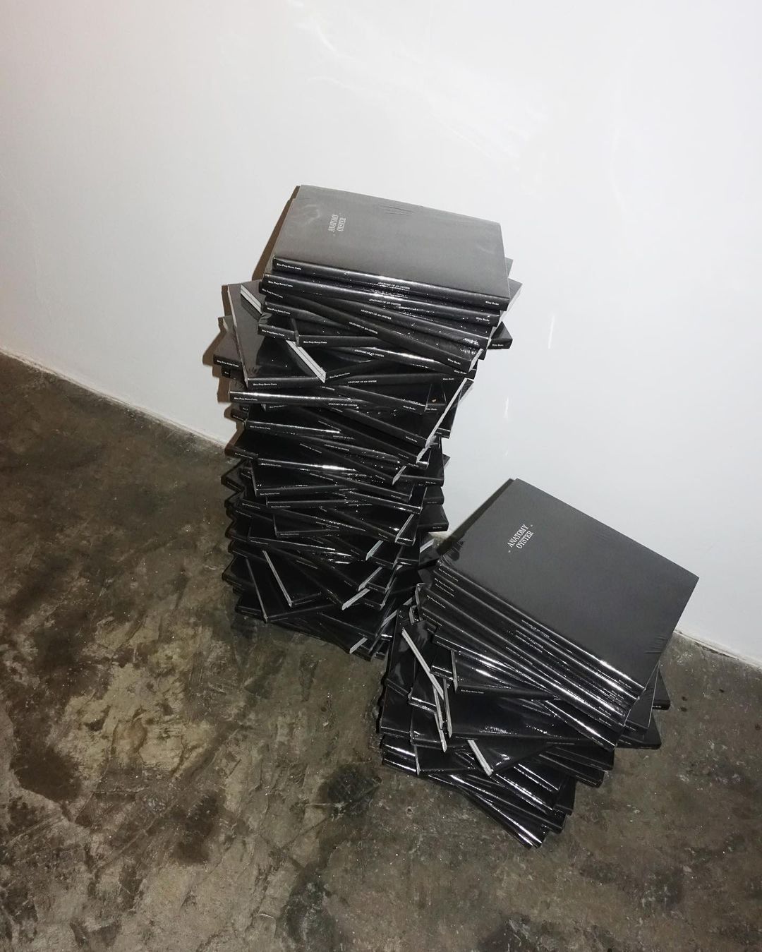 Stack of black hardcover notebooks against a white wall and gray floor, creating a simple and minimalist composition.