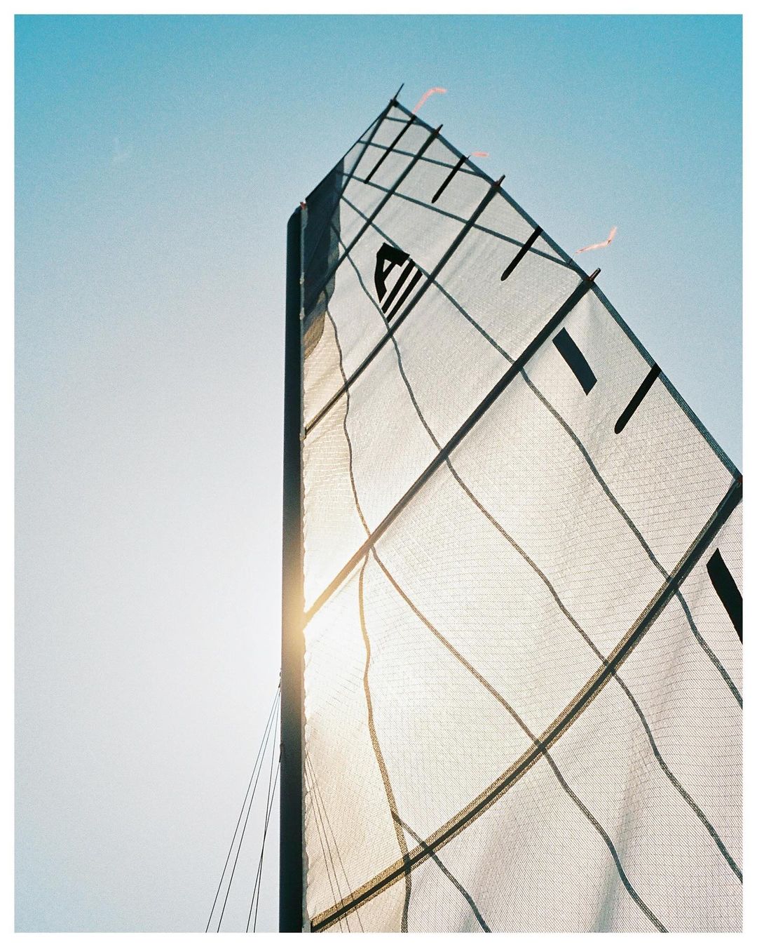 Abstract upward shot of a sailboat sail against a bright blue sky, creating a sense of adventure and maritime activity.