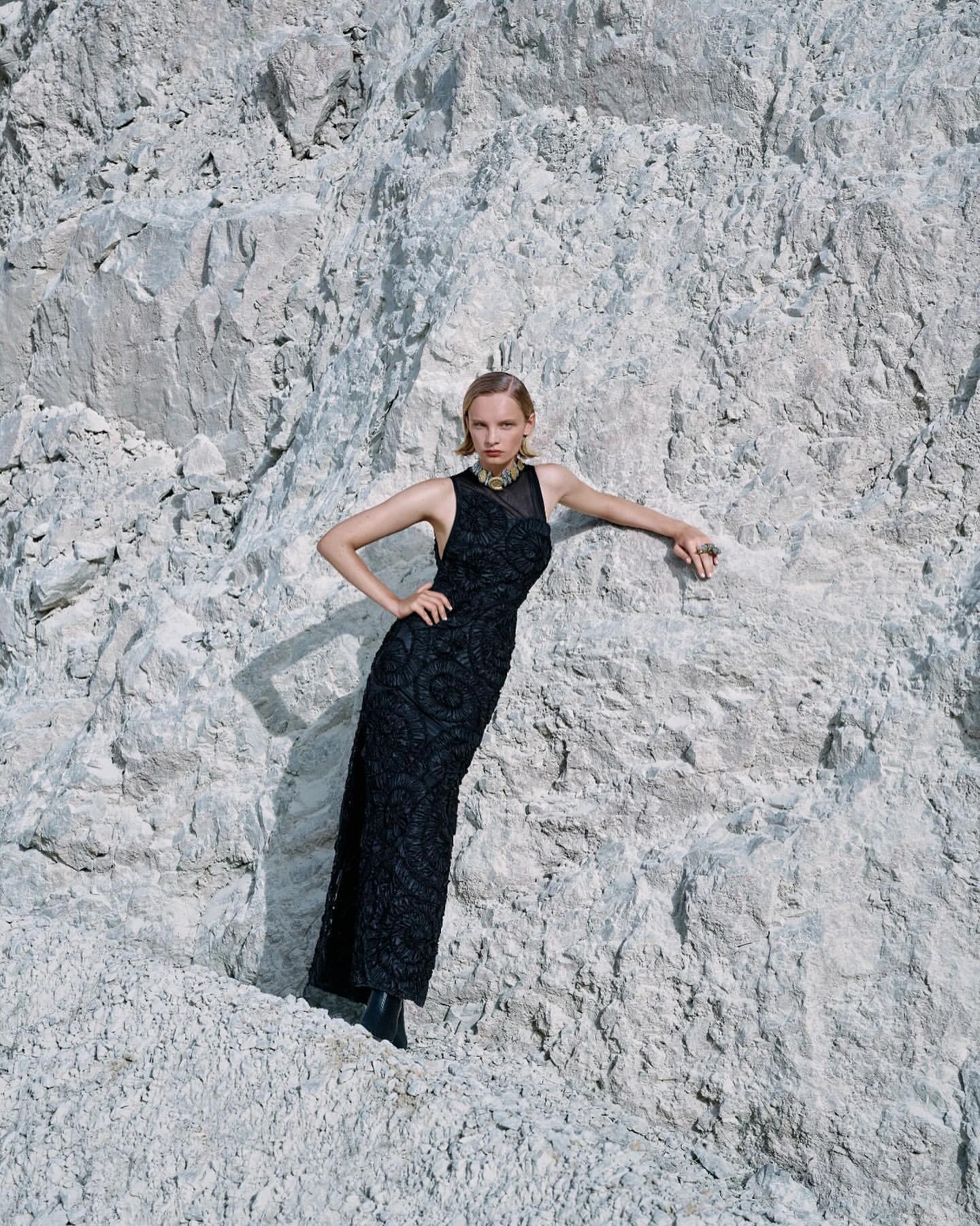 A woman poses in a black gown against a background of white rocks, creating a striking contrast in color and texture.