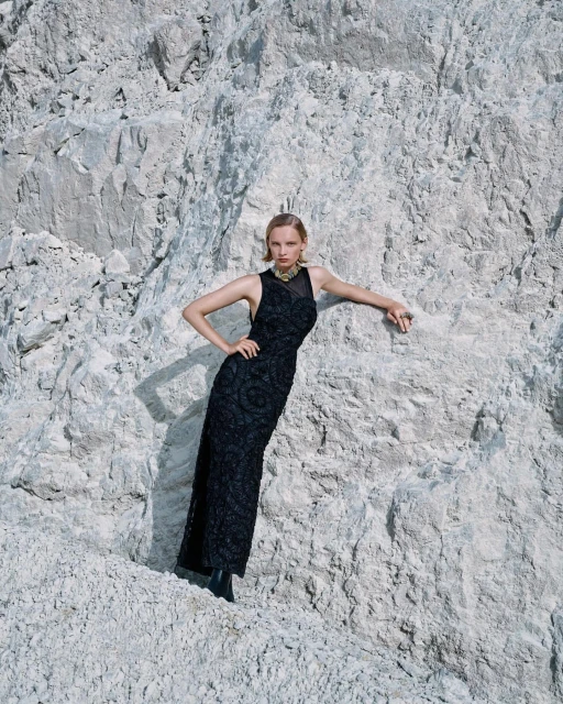 A woman poses in a black gown against a background of white rocks, creating a striking contrast in color and texture.