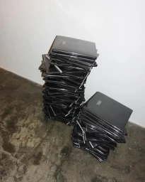 Two tall stacks of black books resting on a rough concrete floor against a plain white wall, photographed by Rita Puig-serra.