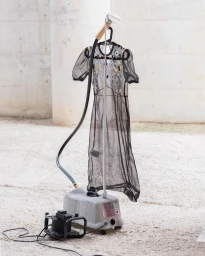 Black sheer embroidered dress hanging on a garment steamer outdoors against a textured concrete wall
