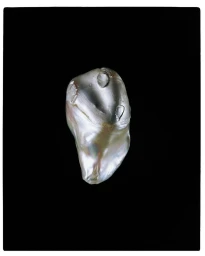 Close-up macro photograph of a single irregular baroque pearl against a solid black background.