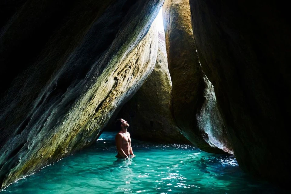 Man stands in turquoise water surrounded by massive rock formations, bathed in natural light, creating a serene and picturesque scene.