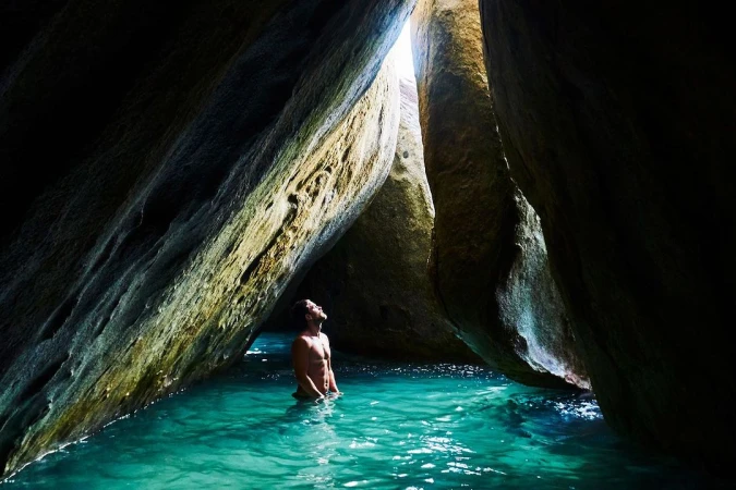 Man stands in turquoise water surrounded by massive rock formations, bathed in natural light, creating a serene and picturesque scene.