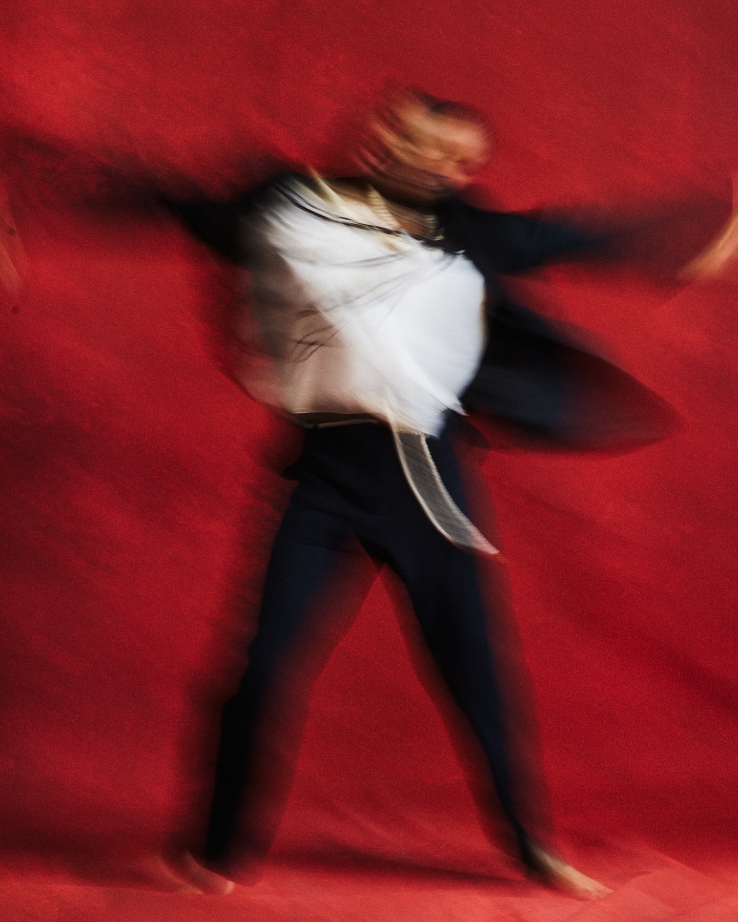 Abstract blurred studio shot of a dancer in motion against a vivid red background, showcasing artistic movement and visual texture.