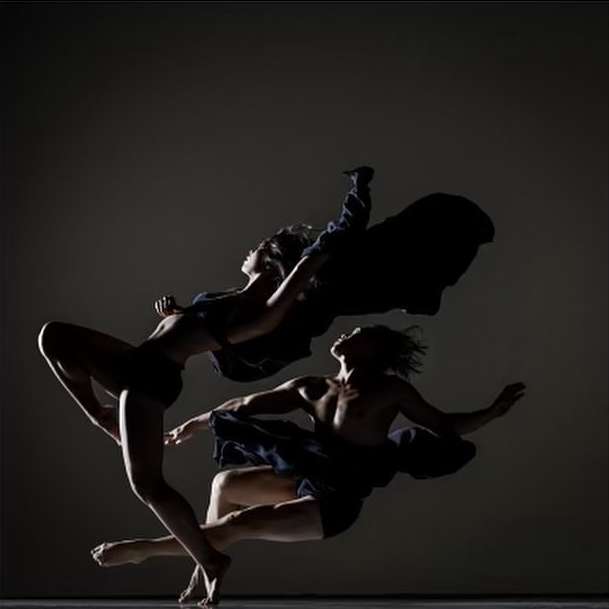 Two dancers strike a pose against a dark background in elegant blue costumes, motion blur accentuating the movement in a modern dance style.