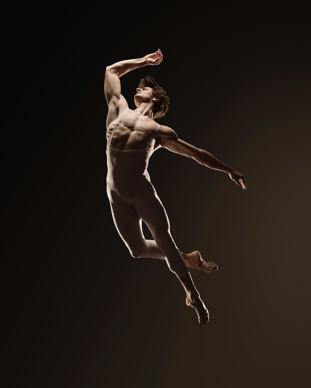 Male ballet dancer in mid-air jump, dark background, dramatic lighting, athletic physique, performing arts, studio shot.