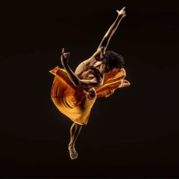 Male dancer captured mid-air leaping against a dark background wearing a draped yellow fabric wrap