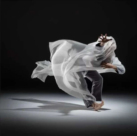 Dancer in motion draped in flowing white fabric against a dark studio background, captured by Rj Muna