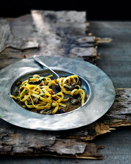 Rustic plate of tagliatelle pasta with mushrooms and herbs on weathered wood surface. Food photography highlighting natural textures.