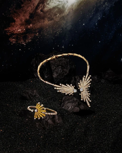 High-end jewelry still life: A gold necklace and ring with diamond embellishments are displayed against a cosmic nebula background.