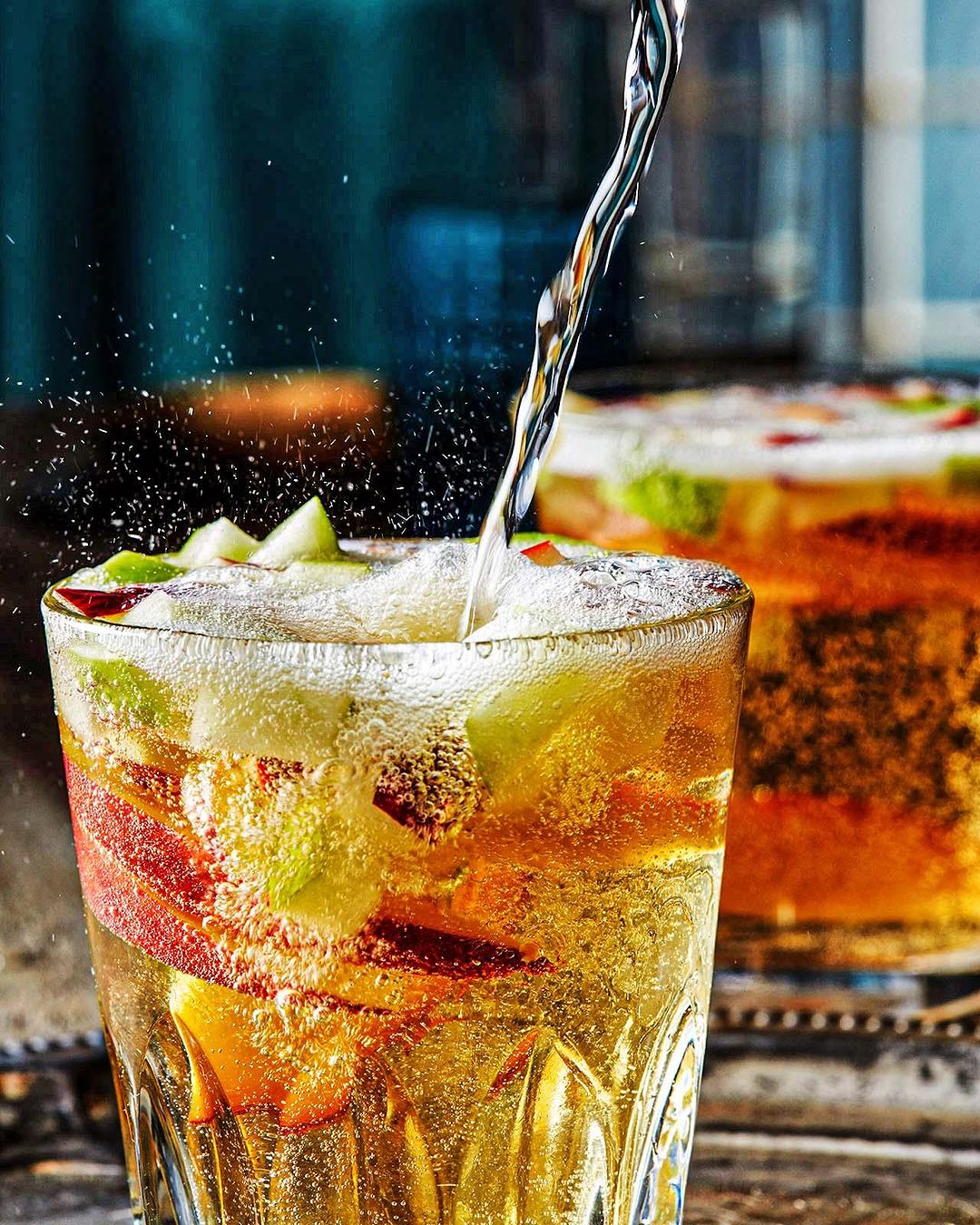 Pouring sparkling liquid into a glass filled with sliced apples and peaches, showcasing a refreshing drink with a bubbly texture.