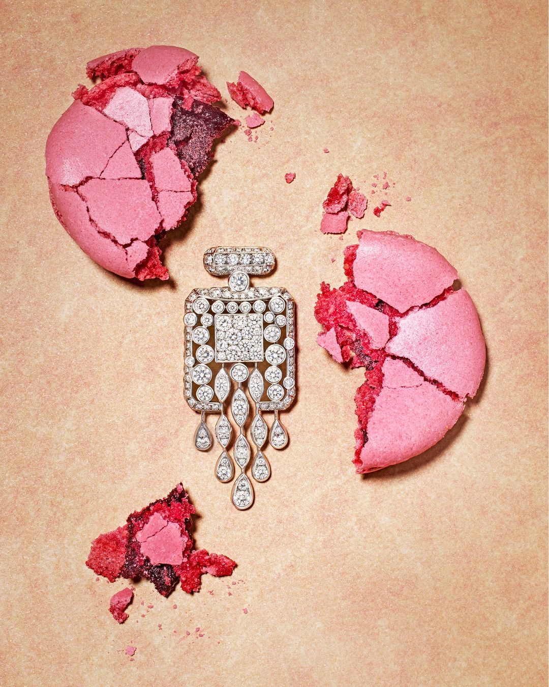 Jewelry perfume bottle pendant surrounded by broken pink macarons on a peach background, advertising luxury jewelry and confectionary.