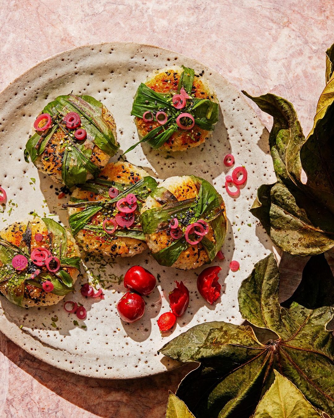 Overhead shot of meticulously arranged food on a speckled plate, garnished with green leaves and red onions, set against a pink backdrop.