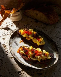 Two slices of egg toast with red roe on a ceramic plate under dramatic side lighting by photographer Rob Fiocca