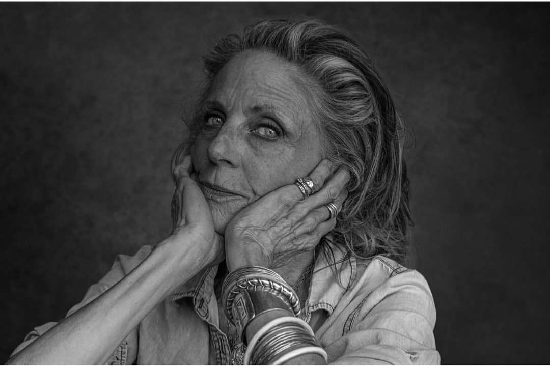 Striking black and white portrait of an elderly woman with expressive eyes, resting her face in her hands, showcasing detailed skin texture.