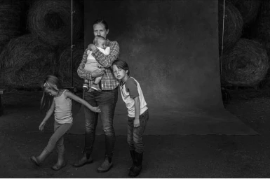 Black and white portrait of a woman holding an infant with two young children by photographer Rob Howard