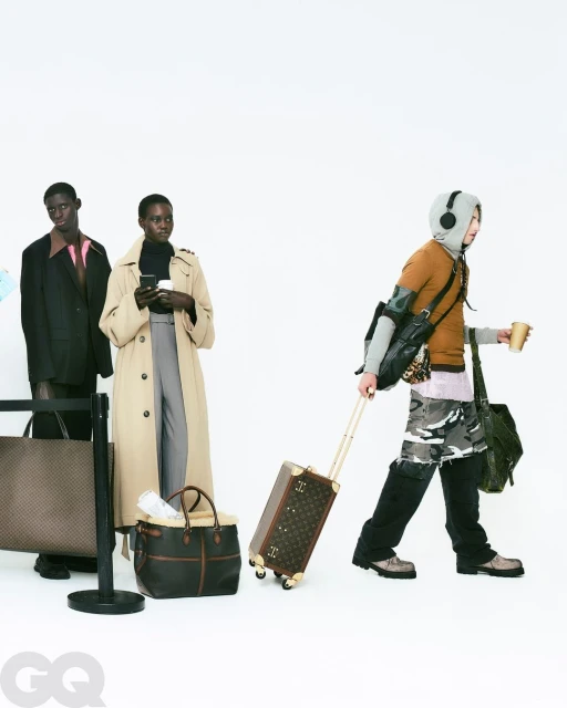 Three models stand in a white studio with luggage; one model is holding a phone, one is holding a cup and has headphones on.
