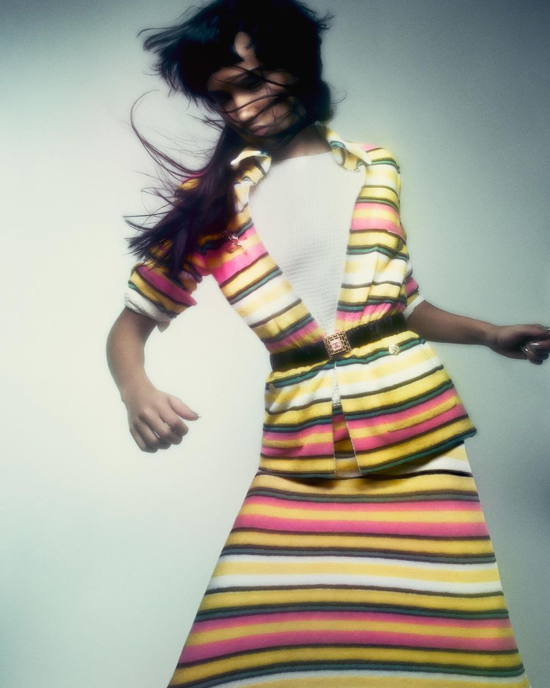 Woman wearing a striped cardigan and skirt with hair blowing across her face against a neutral background