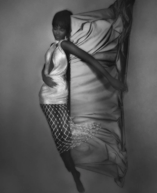 Elegant portrait of a Black woman in a shimmering dress lying next to flowing fabric, captured in a studio setting.