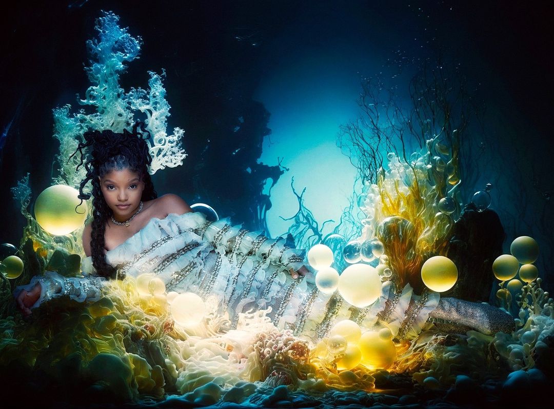 A portrait of a black woman with dreadlocks laying in what appears to be an underwater grotto surrounded by yellow bubbles.