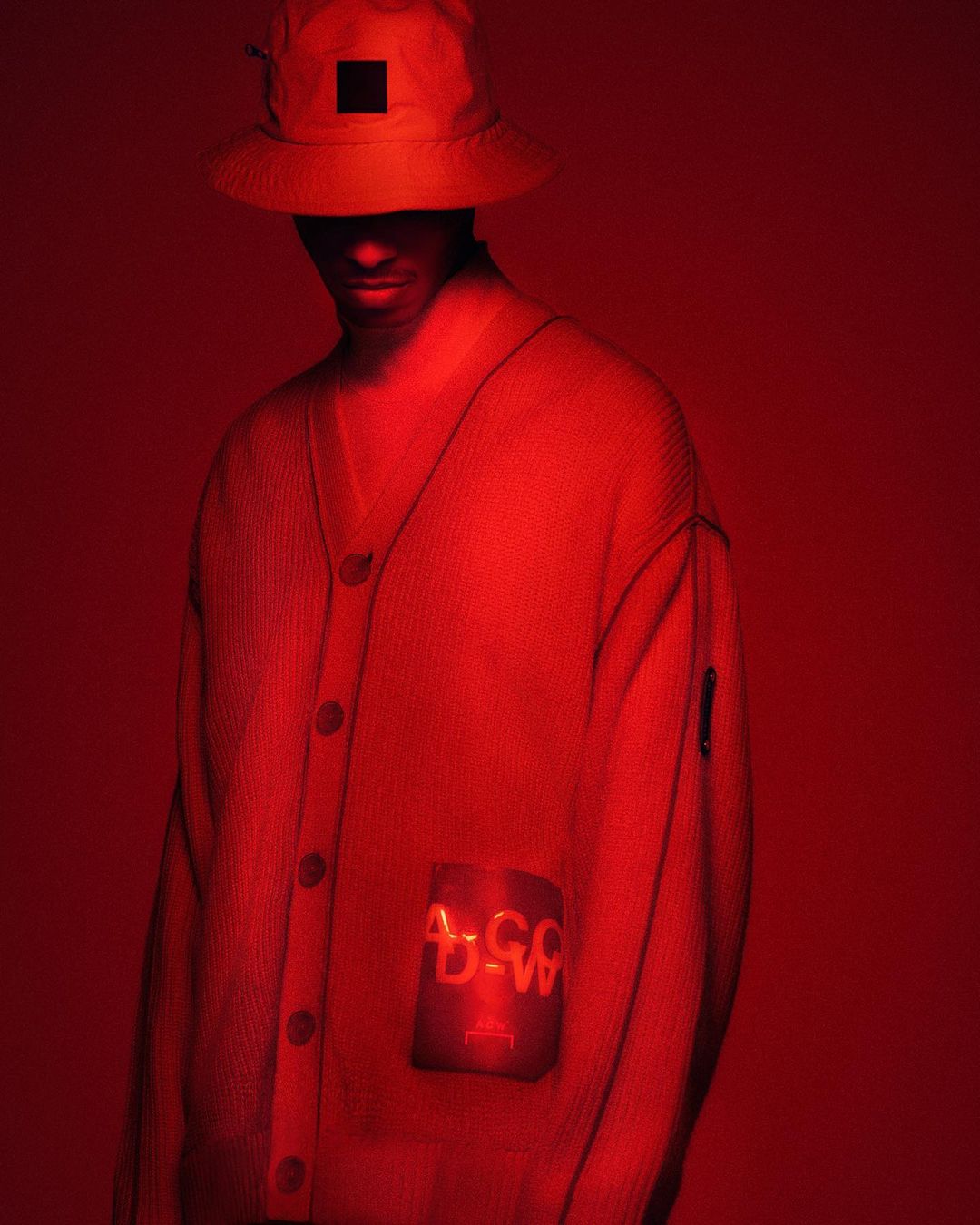 A stylish adult in a red bucket hat and matching red cardigan against a solid red backdrop, captured in a studio setting.