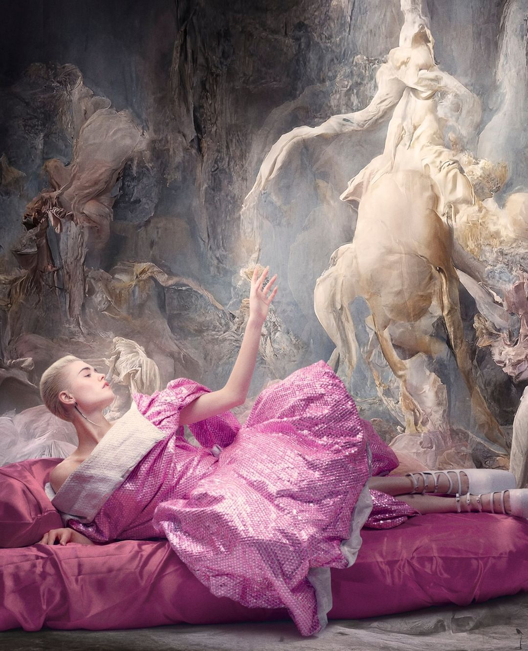 A fair-skinned young woman with short blonde hair lies on a pink bed in a sparkling pink dress with a cream-colored collar, in a fantasy scene.