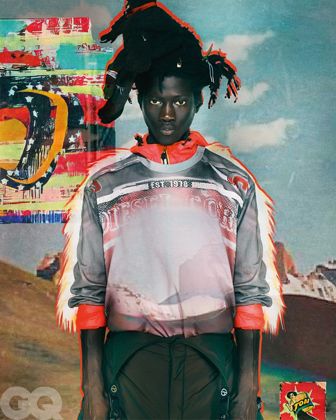Portrait of an adult male fashion model wearing a Diesel top with mountain graphics and dark pants, against a backdrop of illustrated mountains.