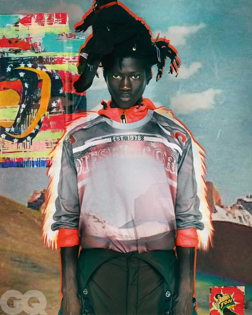 Portrait of an adult male fashion model wearing a Diesel top with mountain graphics and dark pants, against a backdrop of illustrated mountains.