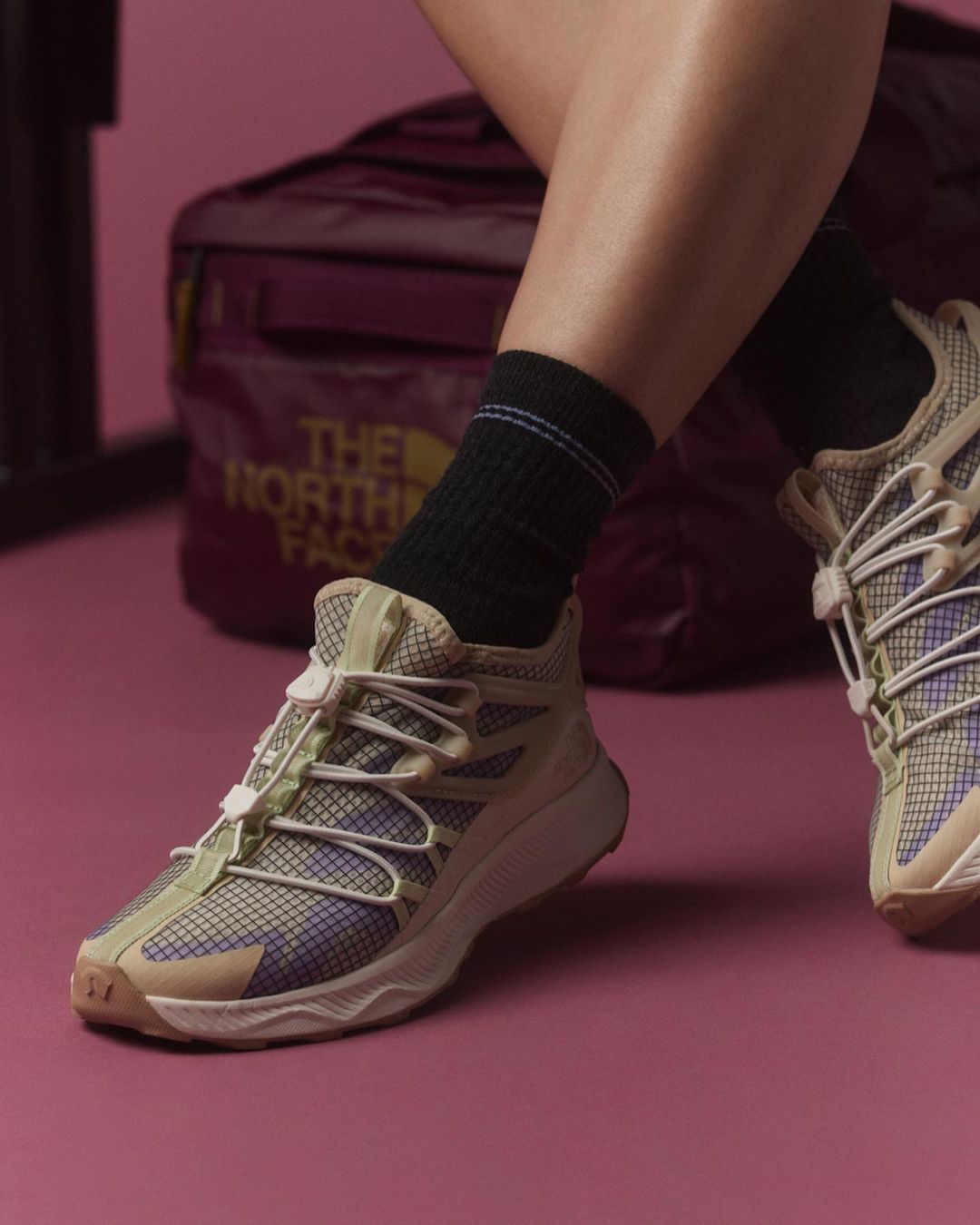 Close-up of beige-colored running shoes with a bungee lacing system and black socks, with a partially-visible burgundy bag in the background.