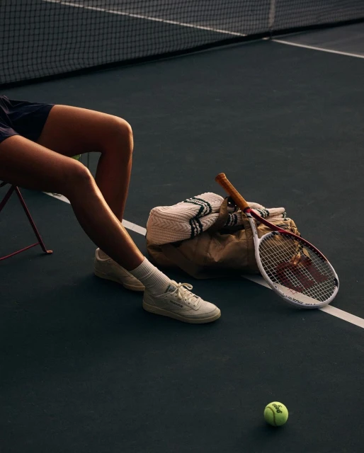Person relaxing on a tennis court next to a tennis racquet and tennis ball in soft lighting. Recreation and sports concept.