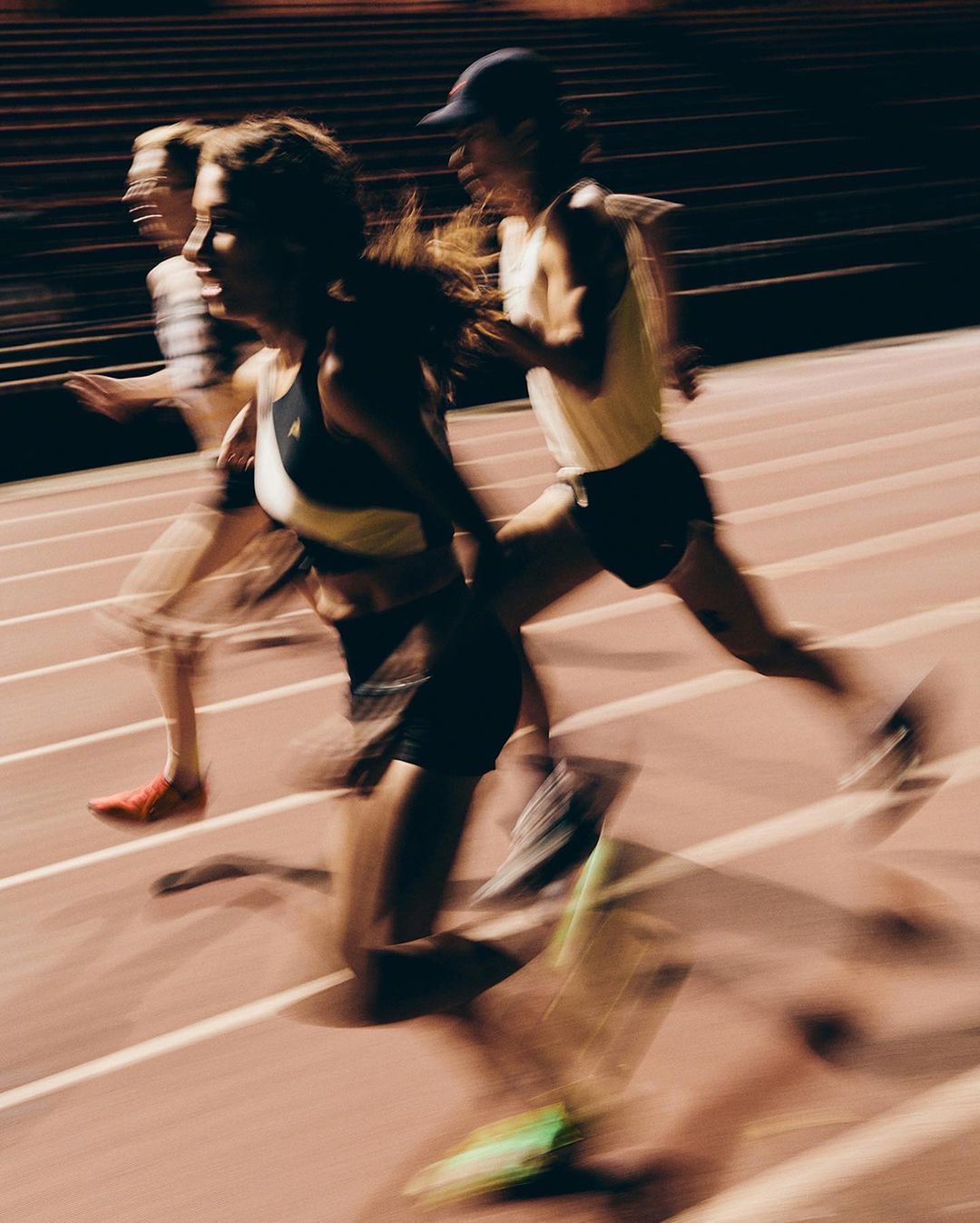 Three female athletes running on a track at night with motion blur, illuminated by stadium lights, showcasing speed and determination.