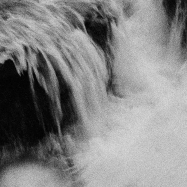 Abstract, close-up black and white photograph of rushing waterfall and water spray against a dark background in a natural environment.