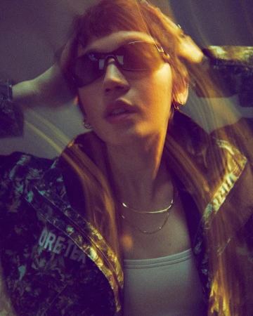 Portrait of a person wearing sunglasses and a patterned jacket with hands behind head by photographer Rob Schanz.