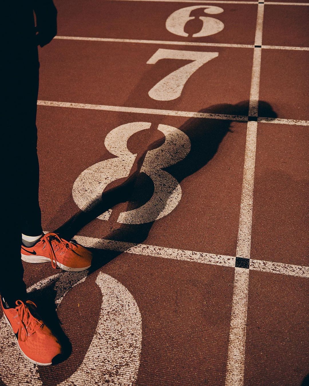 Close-up on a runner's feet in orange sneakers on a red running track with the painted numbers six, seven, and eight.