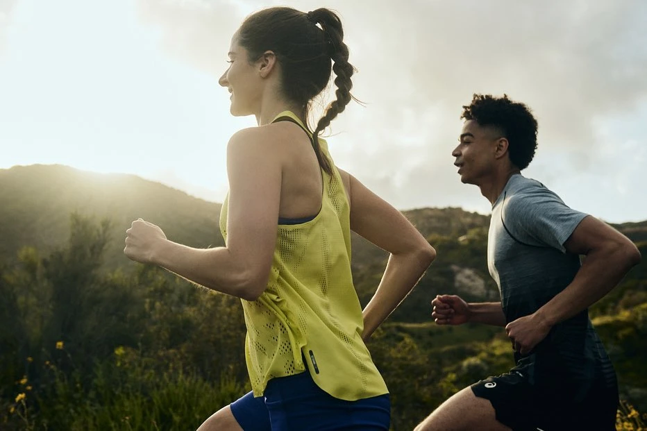 Woman in athletic wear running outdoors with a man, showcasing fitness and healthy lifestyle against a natural green landscape.