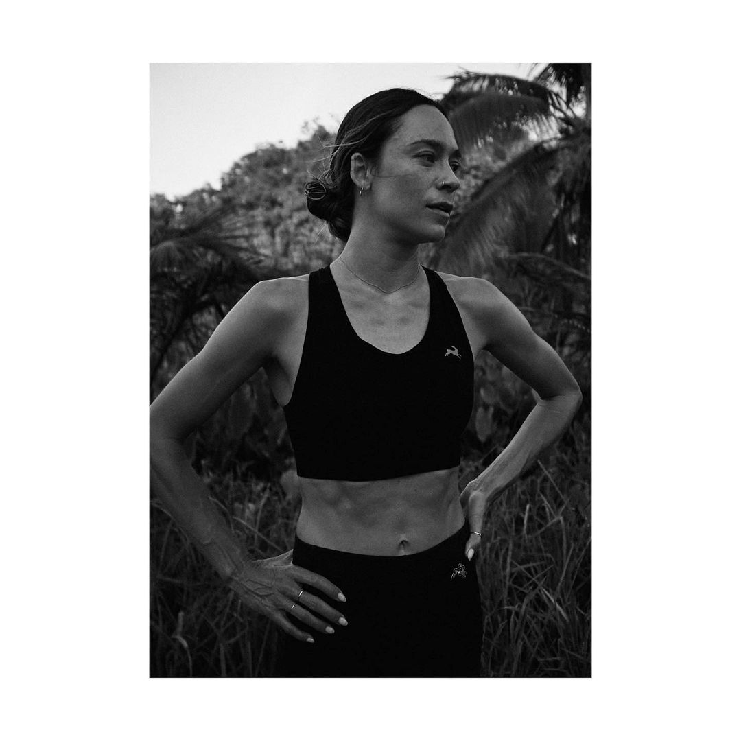 Athletic woman in black workout gear poses in front of a lush, green outdoor background, showcasing strength and natural beauty.
